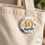 Illustrative canvas bag scene of one 2.25 inch birthday pin button. Sarah and 40 are personalized examples; clothing, bags, wrapping and props not included.
