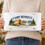 Illustrative size-in-hand view of one 12 x 6 inch decorative aluminum plate. CAMP BENNETT and WEEKEND CREW are personalized examples; mounting hardware and props not included. Not a vehicle registration plate.