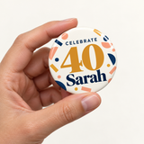 Illustrative size-in-hand view of one 2.25 inch birthday pin button. Sarah and 40 are personalized examples; clothing, bags, wrapping and props not included.